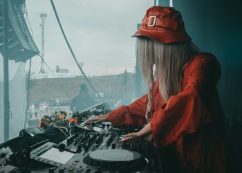 female DJ in red blouse using black DJ software controller during daytime